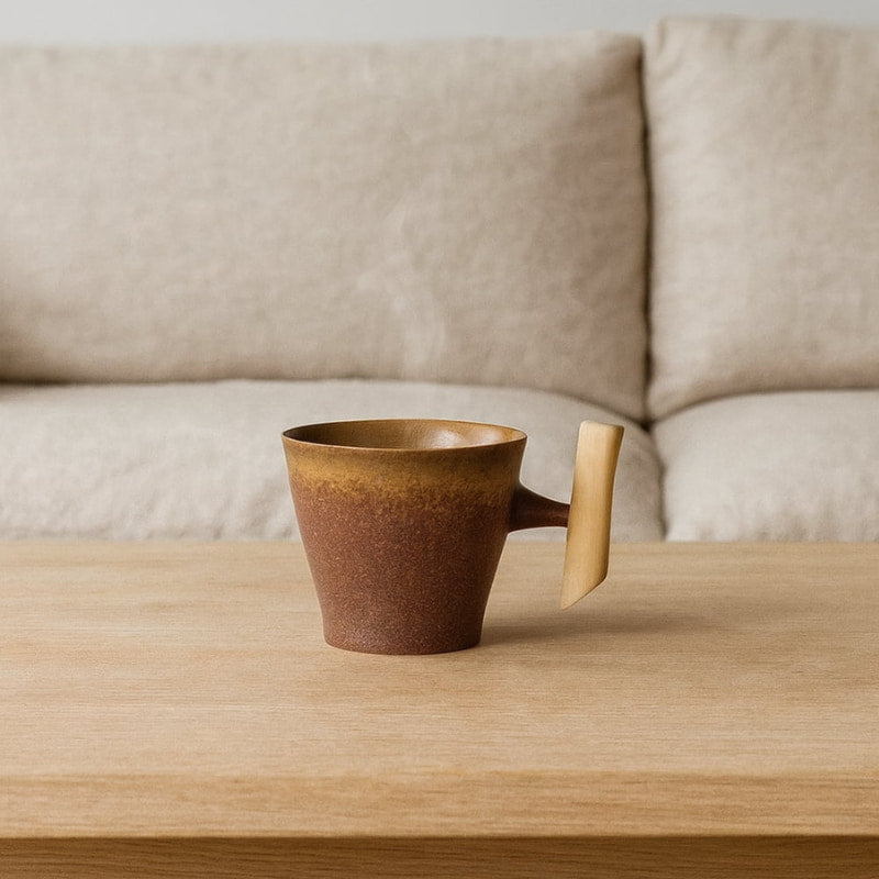 Brown ceramic wabi sabi cup on a wooden table with a beige sofa in the background
