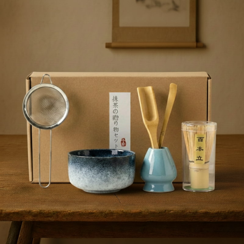 Tea Set Matcha with a box, bowl, whisk, spoon, and glass on a wooden surface.