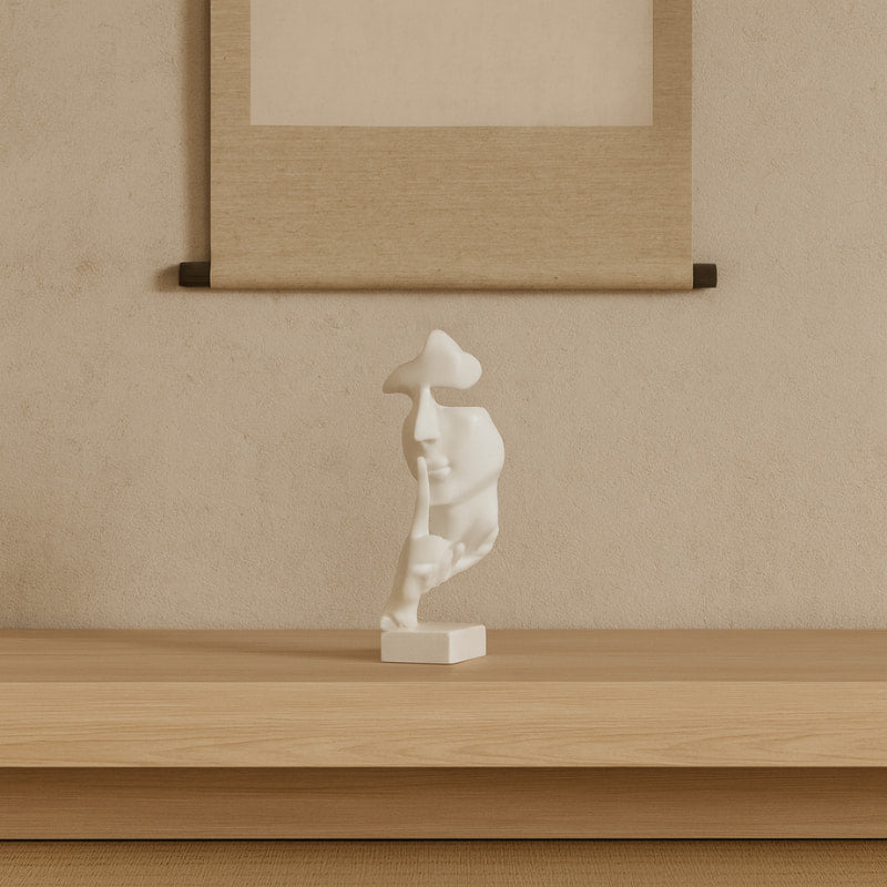 White boho decor sculpture on a wooden shelf with a beige wall and framed artwork in the background