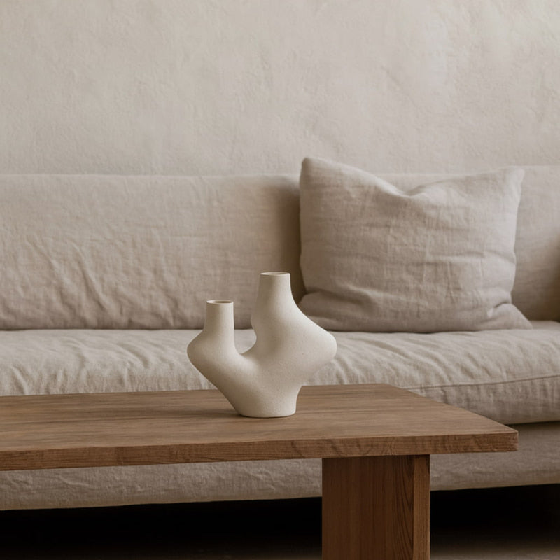 Ceramic handmade vase on a wooden coffee table in front of a beige sofa.