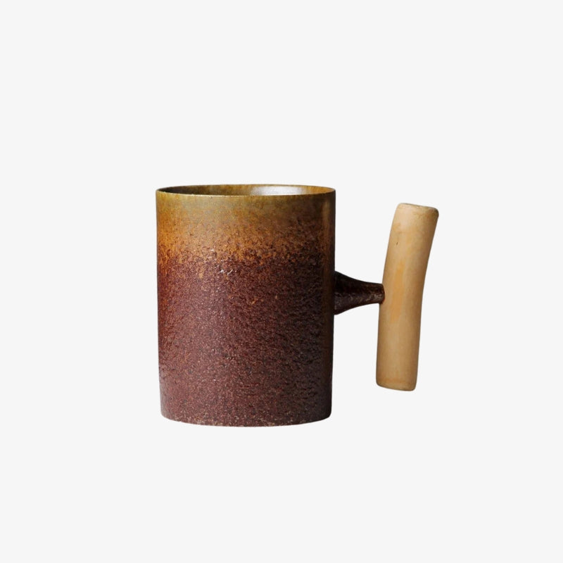 Ceramic tea cup with wooden handle on a textured surface, with a teapot and bowls in the background.
