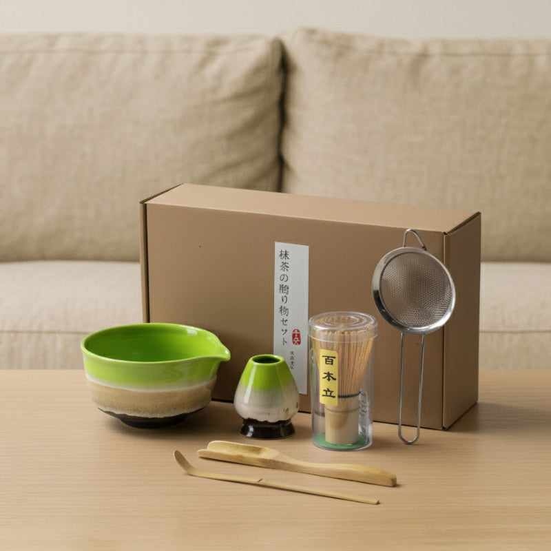 chinese tea set design with a green bowl, whisk, scoop, and other tools in front of a cardboard box.