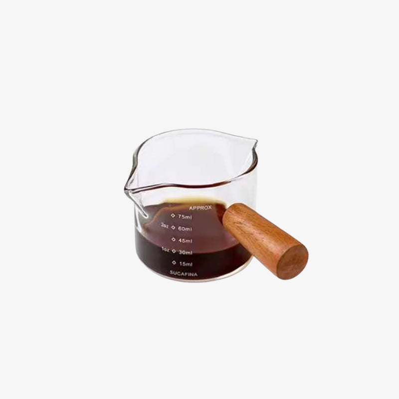 Glass coffee doser with wooden handle containing a dark liquid on a white background