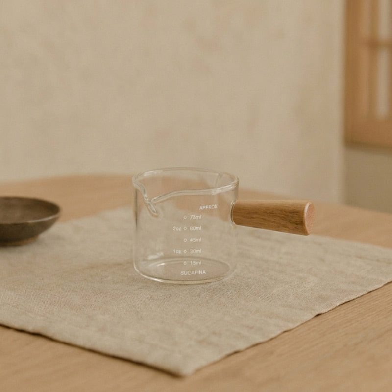 Glass coffee doser with wooden handle containing a dark liquid on a white background