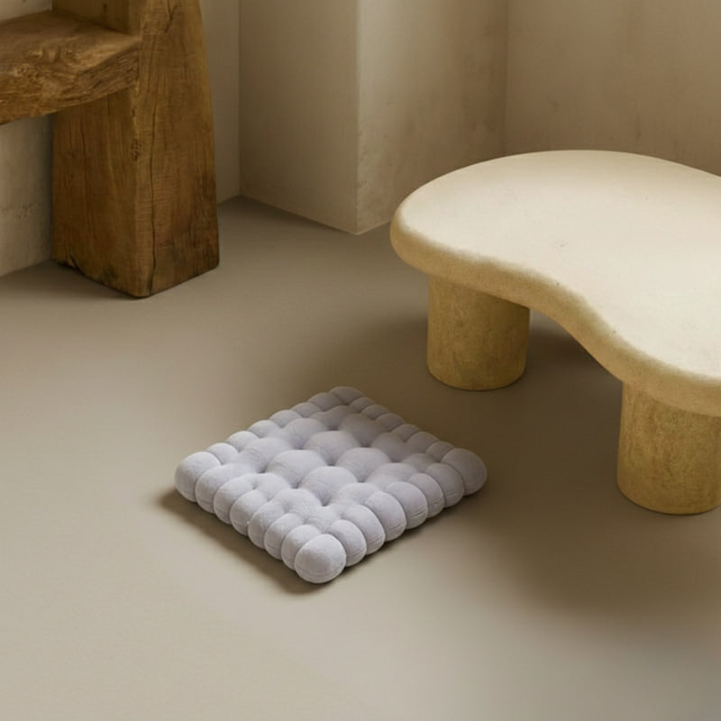 Gray comfy floor pillow on a beige floor with a wooden stool in the background