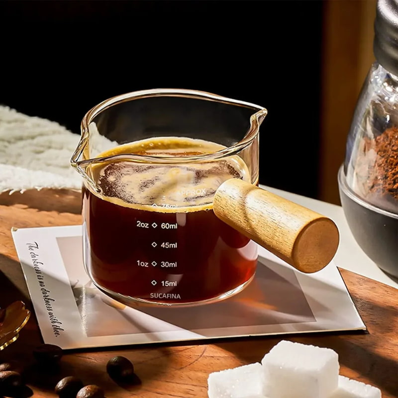 Glass cup measurements with coffee on a wooden surface with coffee beans and sugar cubes.