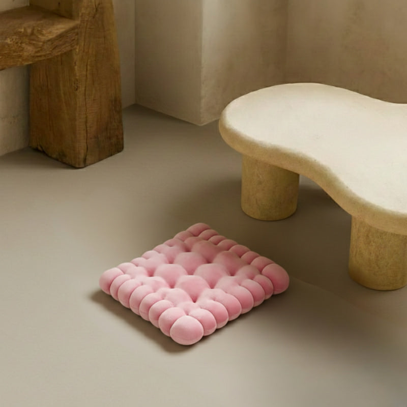 Pink floor seating cushions on a wooden floor with a stone bench and vase in the background.