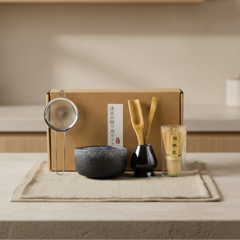 green tea making set with a bowl, whisk, spoon, and glass on a tray with a box in the background.