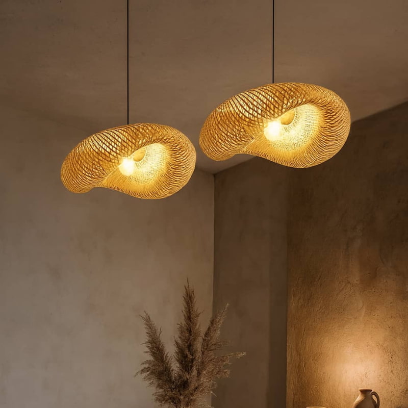 Two hanging bamboo lights against a neutral wall with a plant in the foreground.