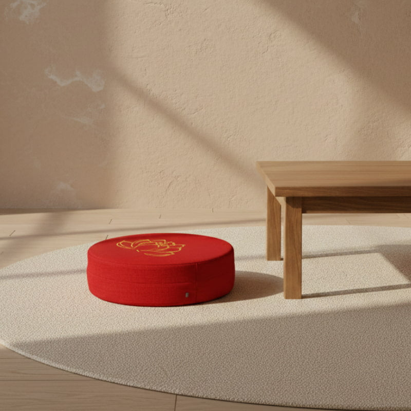 Large red floor cushions with a design on a beige floor next to a wooden table.