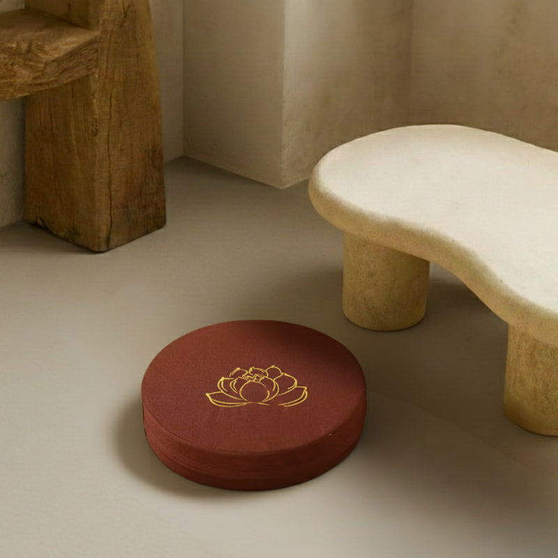 lotus design meditation cushion with a gold lotus design on a beige floor next to a stone bench.