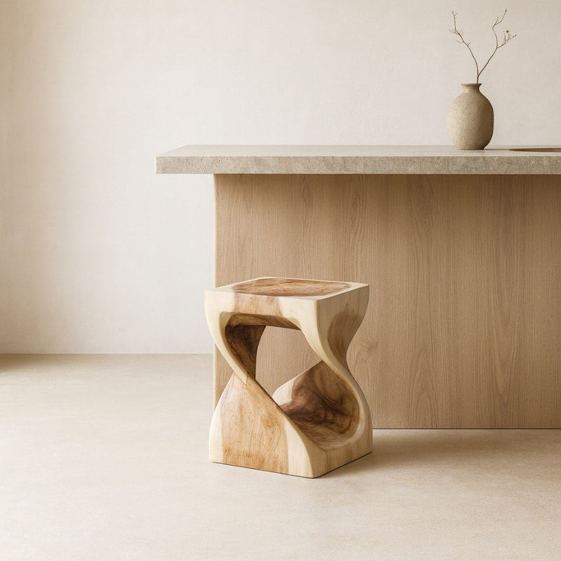 Low stool with white cushion next to a wooden table with a vase on a beige carpet.