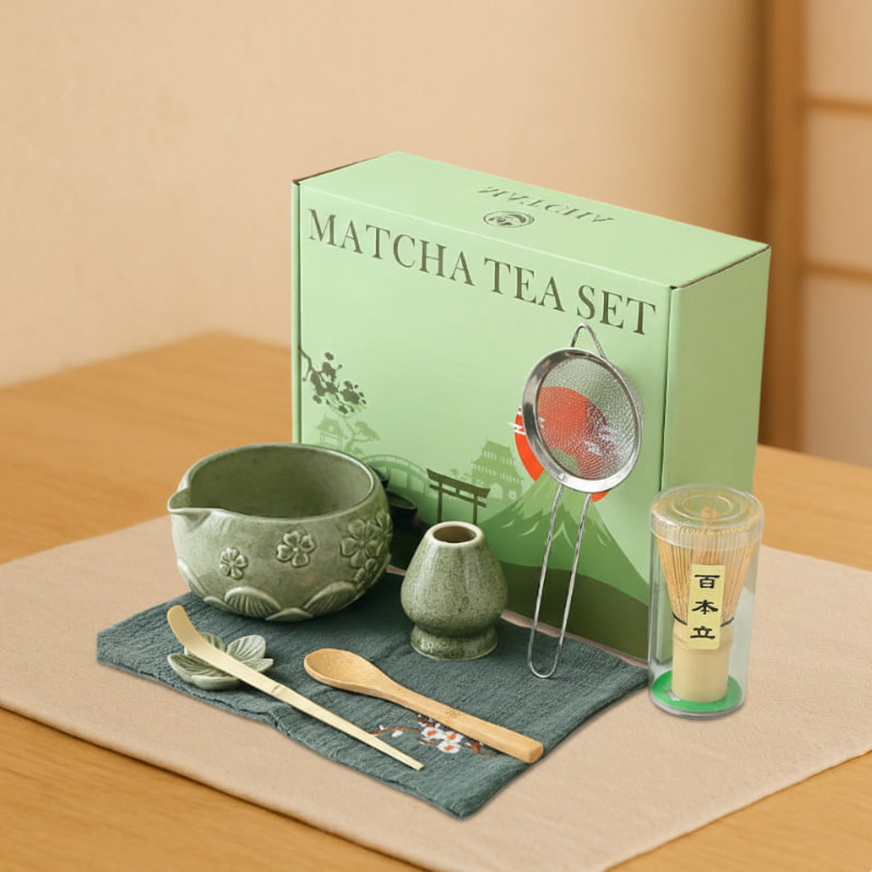 matcha tea gift set with green box, bowl, spoon, whisk, and other tools on a textured surface.