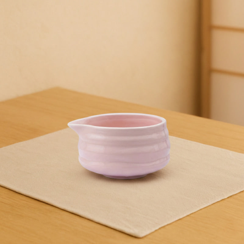 Pink matcha bowl ceramic pitcher on a wooden surface with a beige wall background