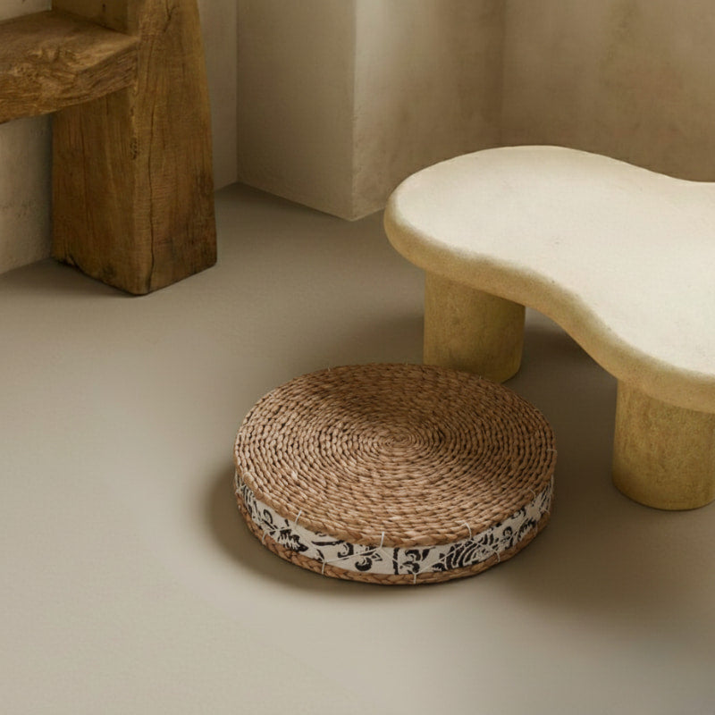 straw floor cushions with floral pattern next to a stone bench on a neutral floor.