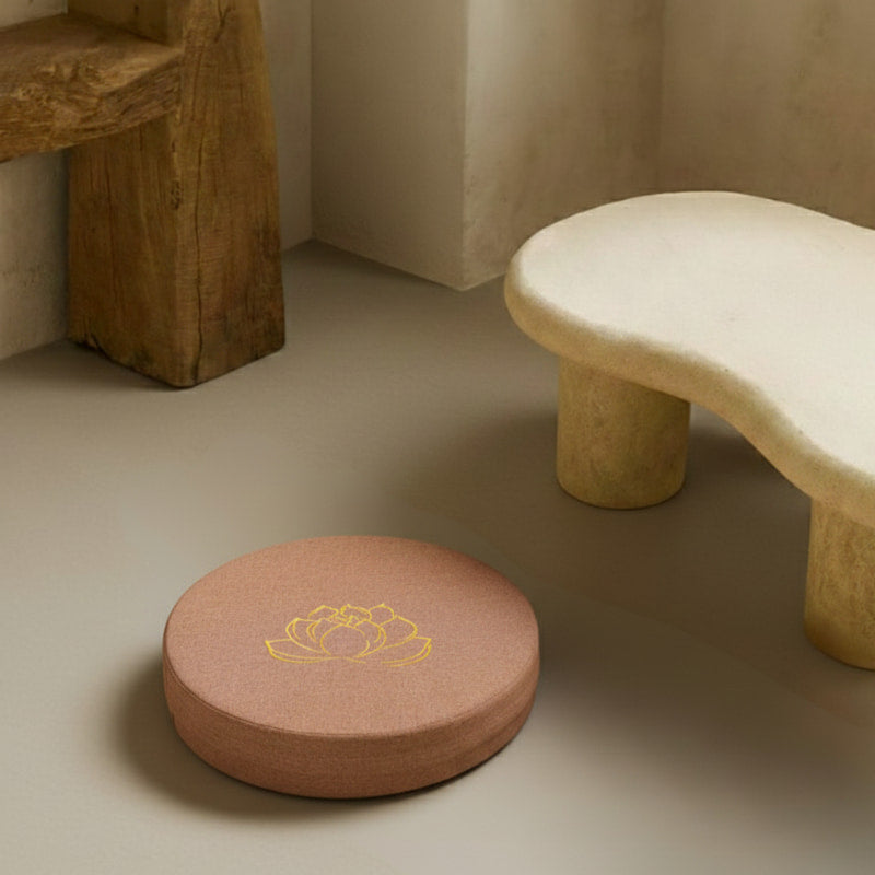 Round terracota cushion with a yellow lotus design on a beige floor next to a stone stool.