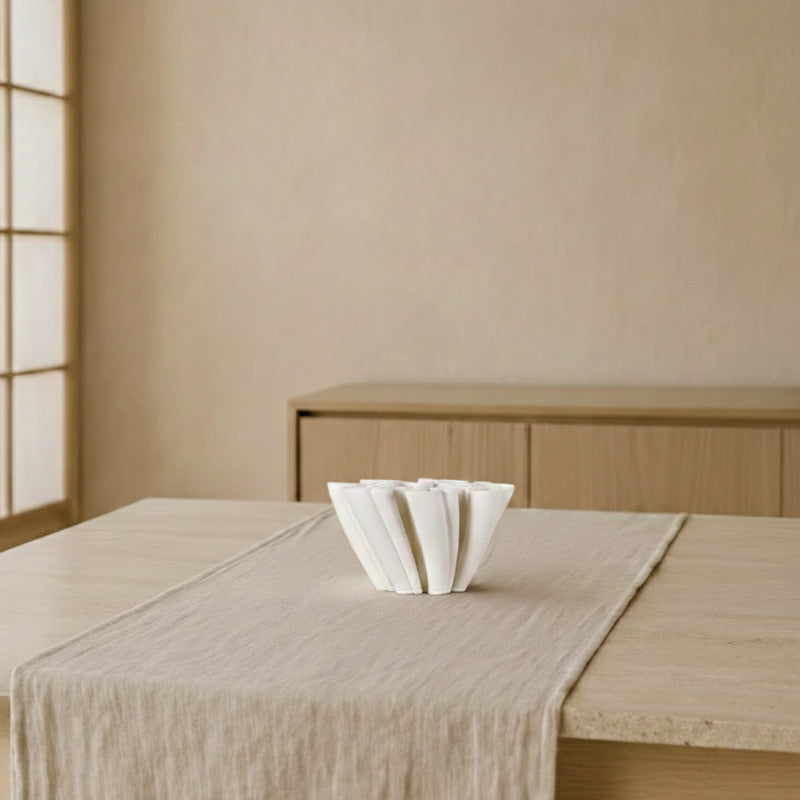 White vase ceramic creative on a textured beige tablecloth with a wooden cabinet and window in the background.