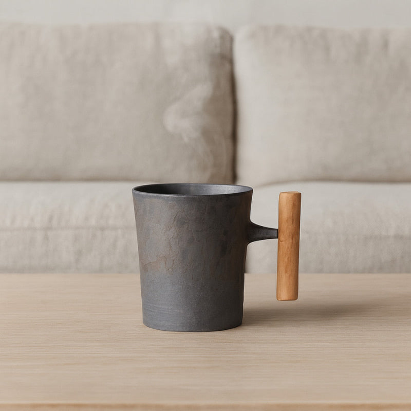 Dark vintage mug with a wooden handle on a wooden surface with a light gray sofa in the background.