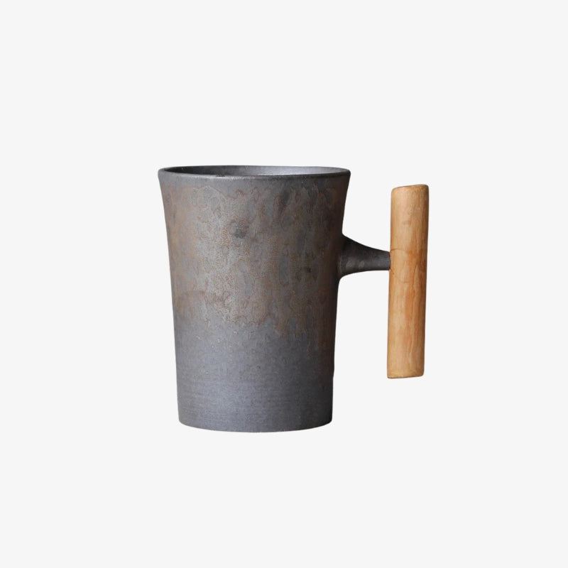 Wabi sabi tea mug with wooden handle on a textured surface with teapot and bowl in the background.