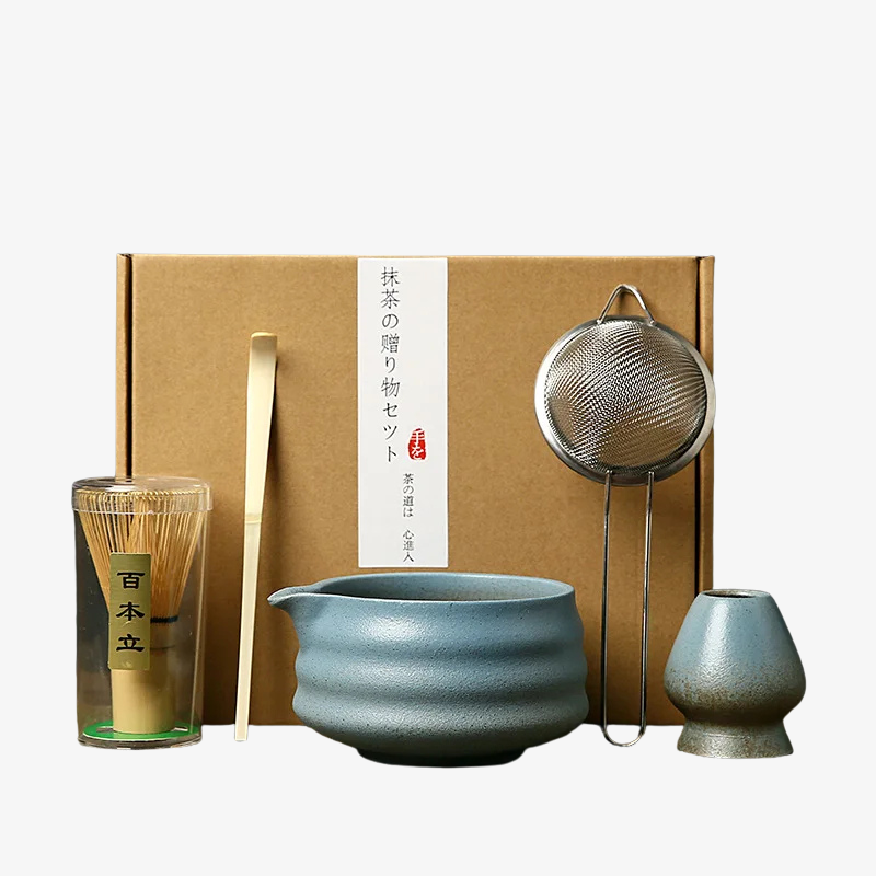 Tea-making whisk set matcha with a blue ceramic bowl, glass, and other tools in front of a brown box.