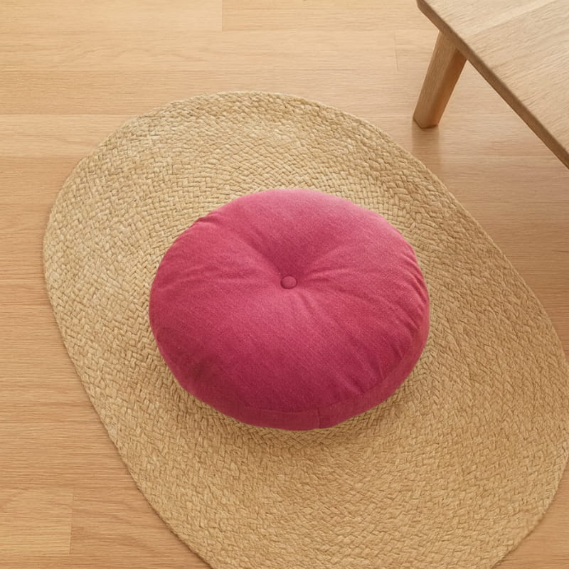 Round pink japanese cushion on a woven mat on a wooden floor