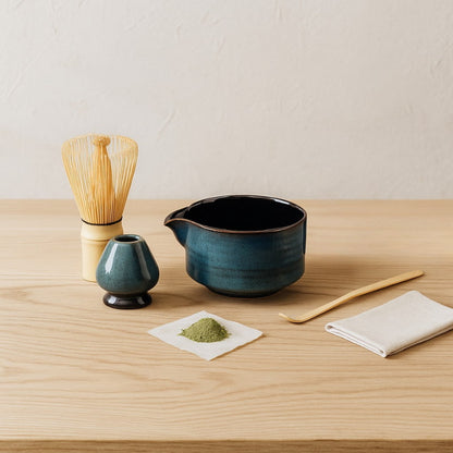 authentic matcha whisk set​​ with blue teapot, whisk, and scoop on a wooden surface.
