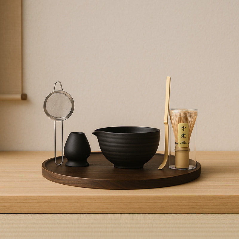 Tea-making set with black bowl, bamboo whisk, and other tools on a wooden tray against a beige wall.