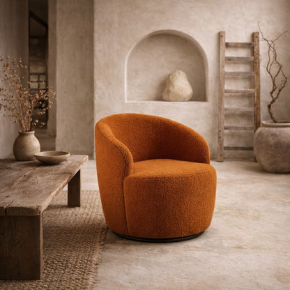 Orange beautiful boucle swivel accent chair​ in a rustic room with wooden table and stone wall.