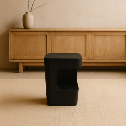 Black wood stool in front of a wooden cabinet with a vase on a beige floor.