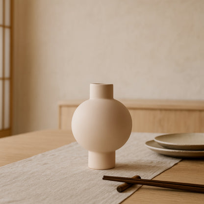 Beige ceramic handmade clay vase​ on a table with a neutral background