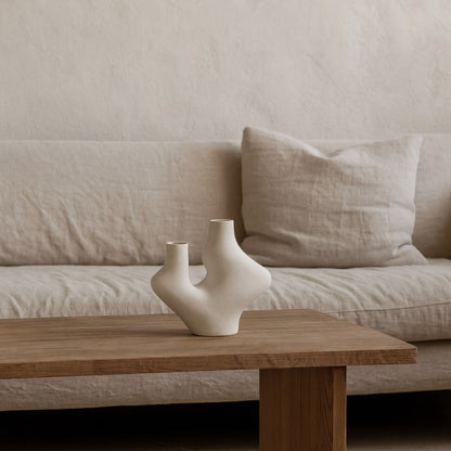 Ceramic handmade vase on a wooden coffee table in front of a beige sofa.