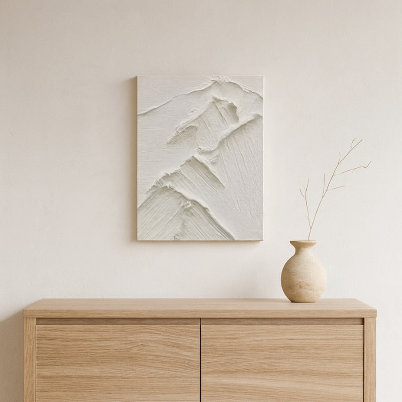 Contemporary wabi sabi art​ piece on a wall above a wooden cabinet with a vase.
