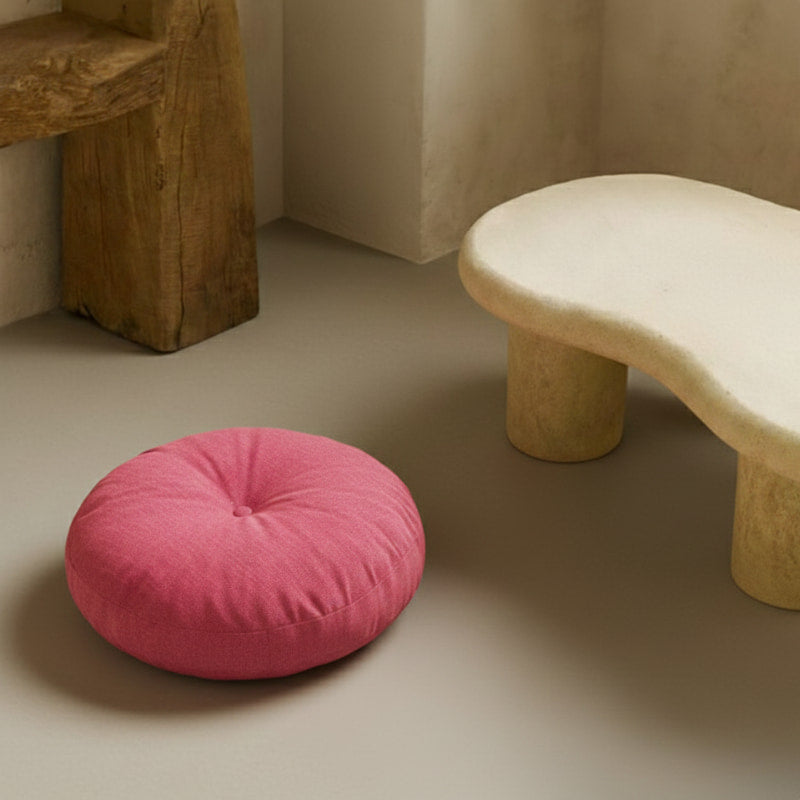 Pink cushioned floor chair on a neutral floor with a textured wall and wooden bench in the background.