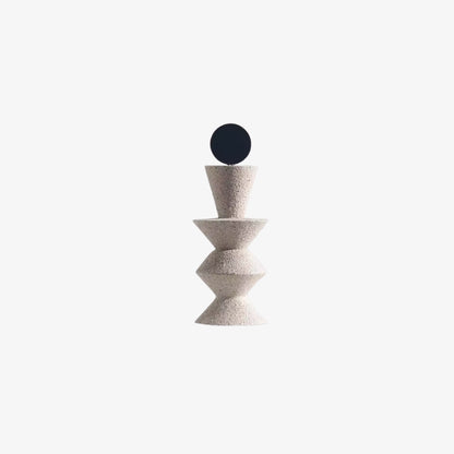 Decorative circle object with a black sphere on top of a textured beige column against a white background