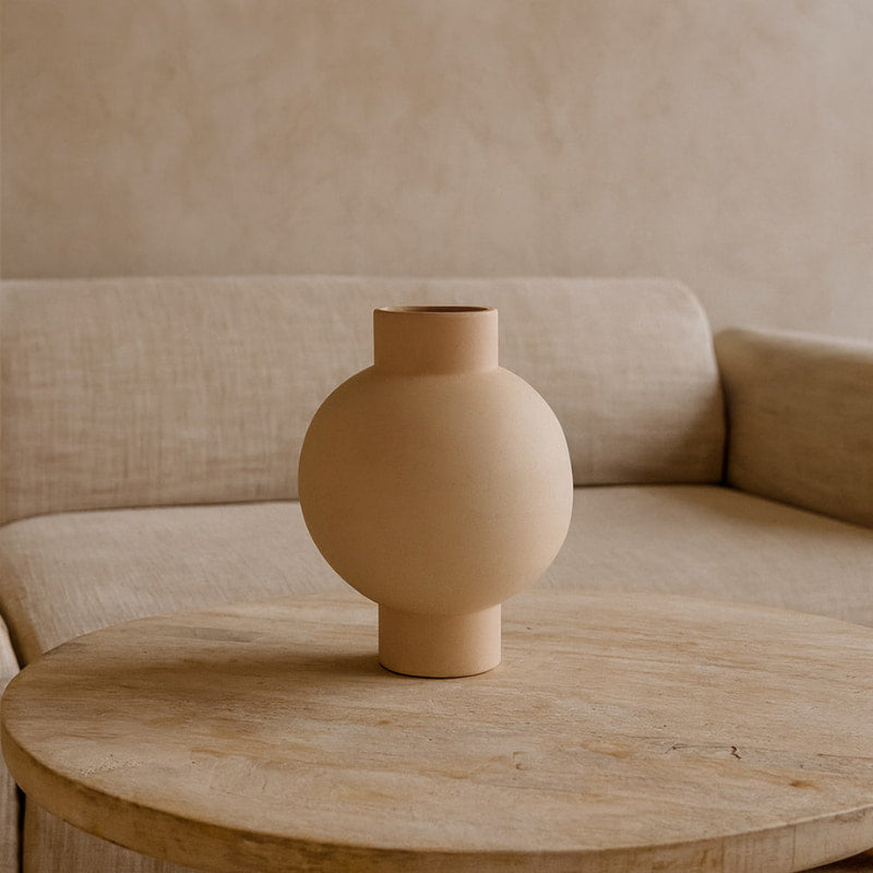 Designed beige vase on a wooden table with a beige sofa in the background