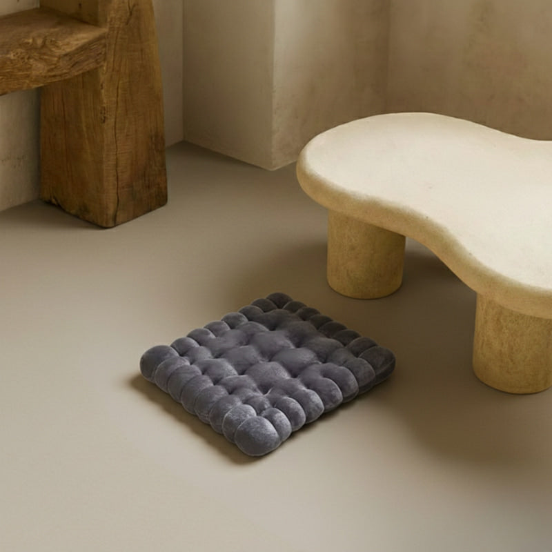 Black floor cushions ikea on a beige floor with a wooden stool and stone bench in the background.