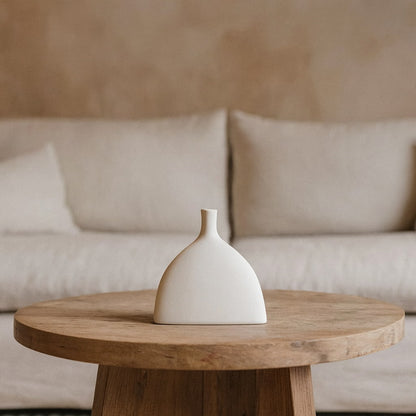 White flower vase aesthetic​ on a wooden table with a beige sofa in the background