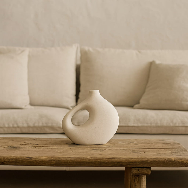 Handmade ceramic vase on a wooden coffee table with a beige sofa in the background