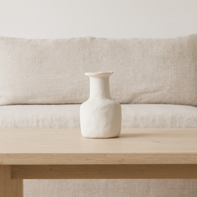 Irregular ceramic vase on a wooden table with a beige sofa in the background