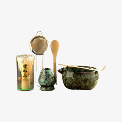 japanese matcha ceremony set​ with green ceramic pot, wooden spoon, and glass container on a white background