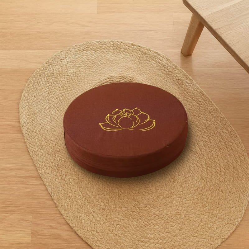 Round brown lotus cushion on a woven mat on a wooden floor.