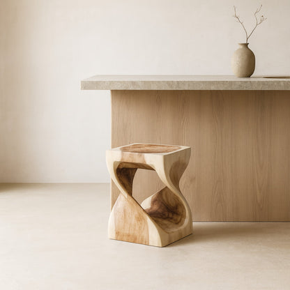 Low stool​ with white cushion next to a wooden table with a vase on a beige carpet.