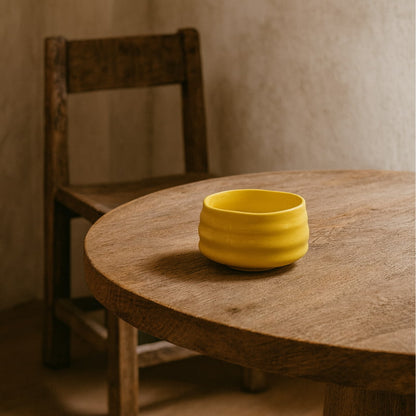 Yellow ceramic matcha bowl clear on a wooden table with a rustic chair in the background.
