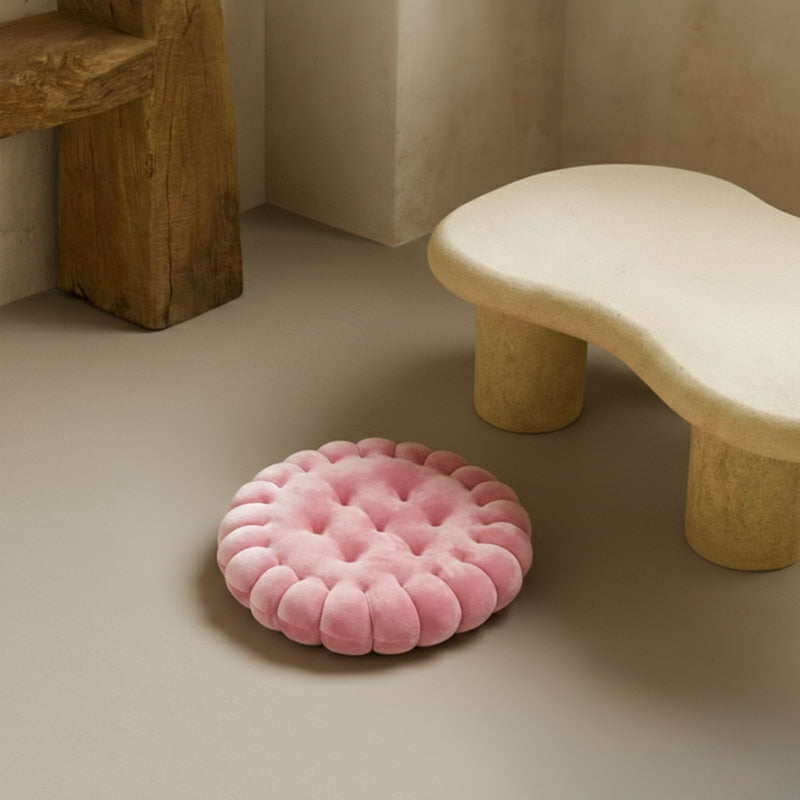 Pink floor cushion on a textured floor with a stone bench and vase in the background.