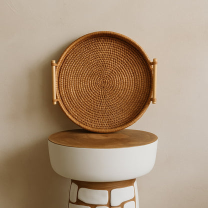 Woven rattan oval tray​ with handles on a white pedestal against a beige background