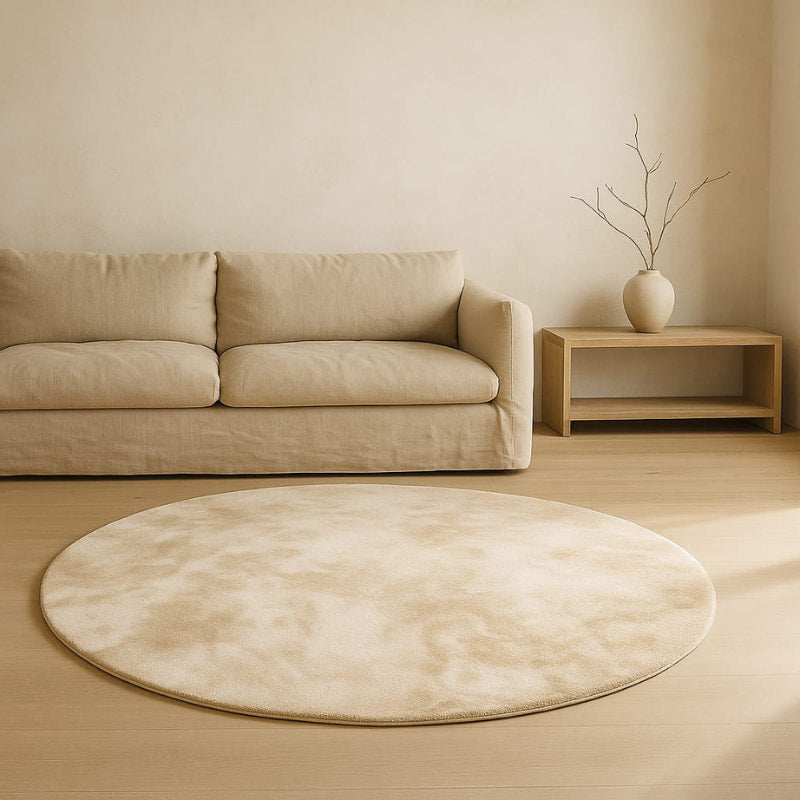 Beige living room with a round white carpet​, beige sofa, and wooden side table.