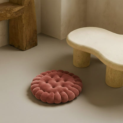 Round pink seat cushion on a neutral floor with a stone bench in the background