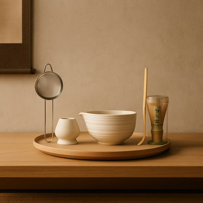 Set for matcha with a bowl, whisk, and other tools on a wooden tray against a beige wall.