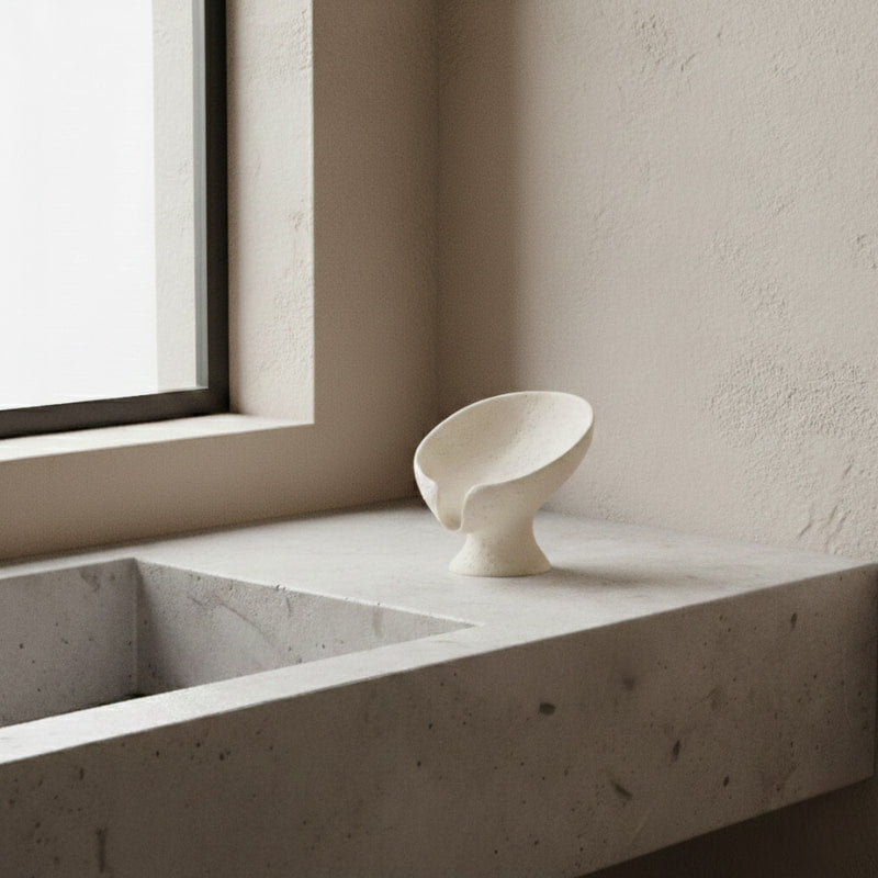 Soap holder white on a concrete surface near a window with a neutral wall.