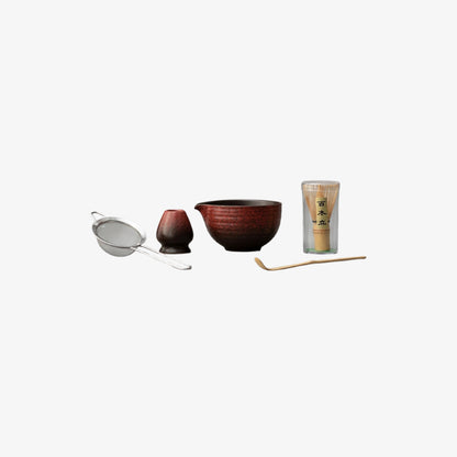 Tea-making set with bowl, strainer, spoon, and glass container on a white background
